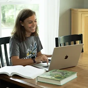 High school student sitting at table smiling while working on laptop