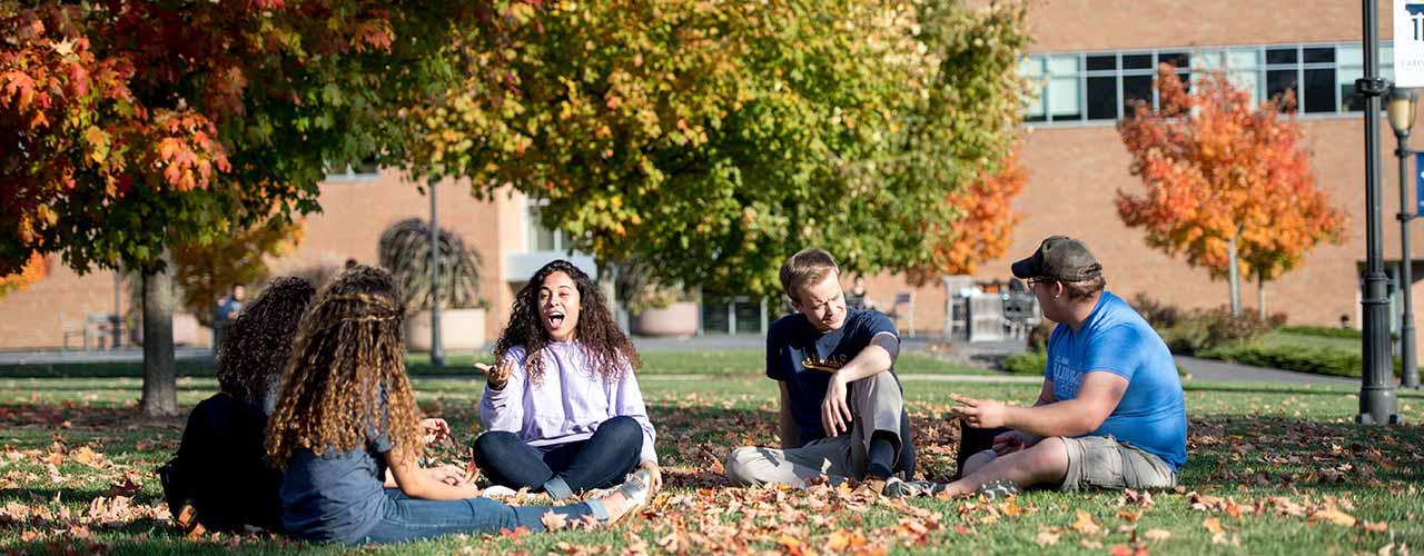 Group of Cedarville students relax in the grass and autumn leaves