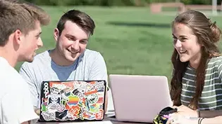 Students studying outside at a table using their laptop computers.