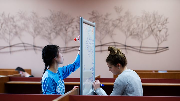 Two students using a double-sided white-board in the library